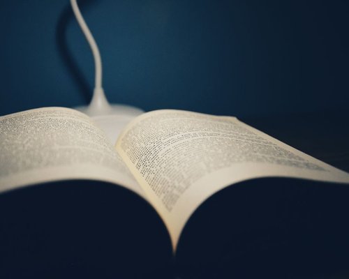 A desk lamp providing warm soft light over an open book at night
